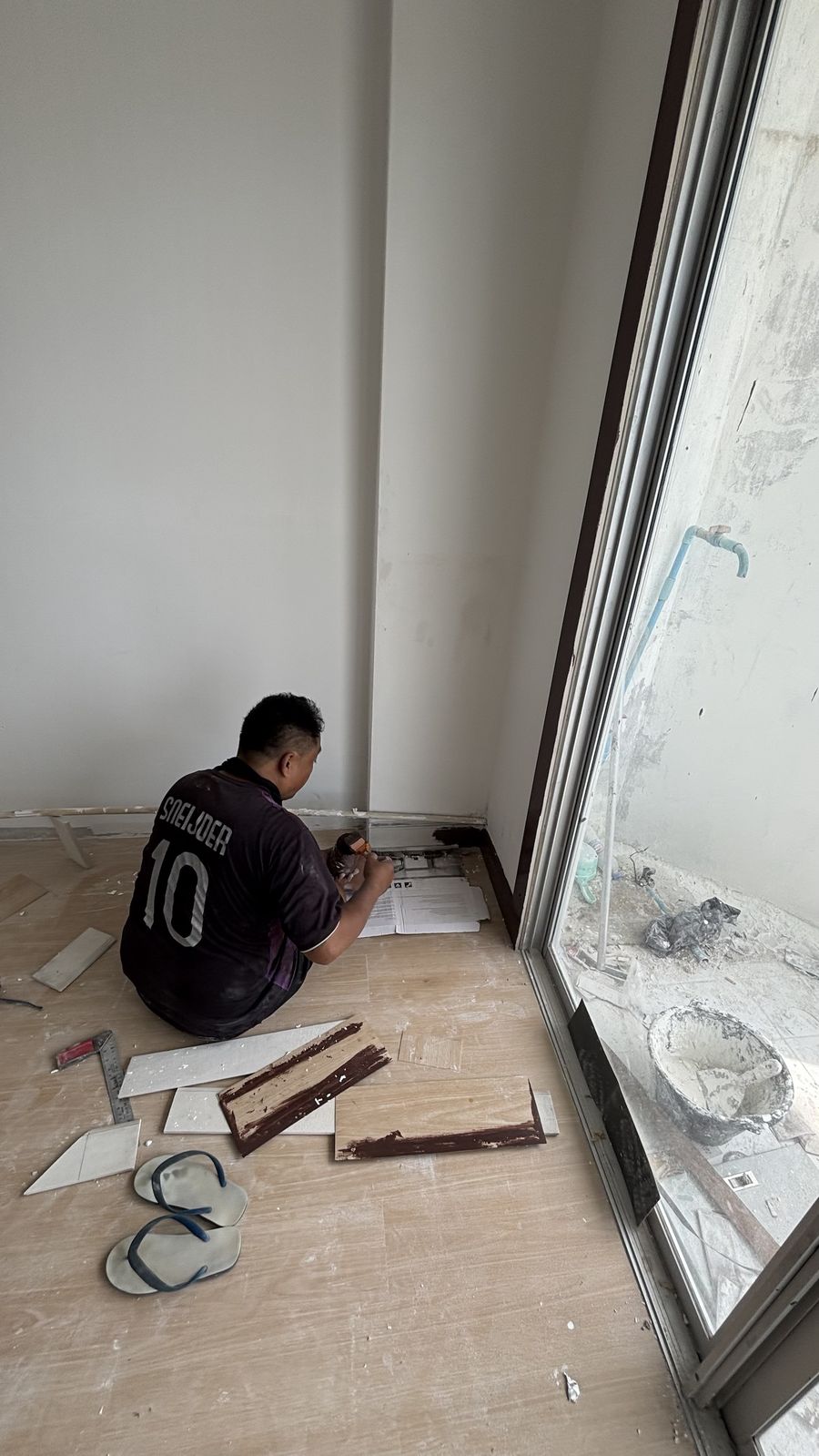 Fitting cut tile skirting beside the balcony door over new wood-look flooring at Chain Condominium, Jomtien