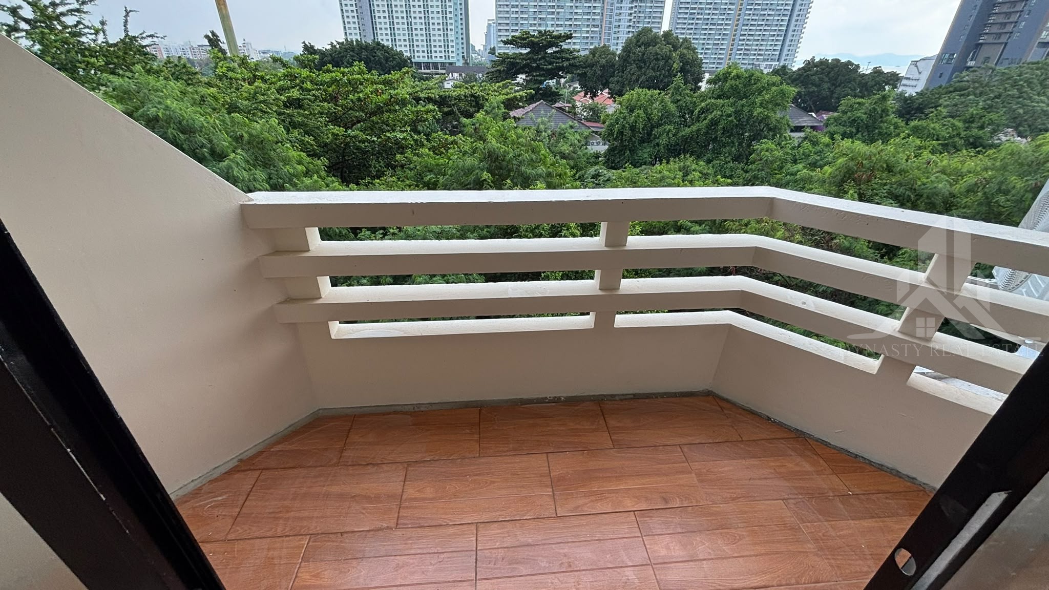 Repainted balcony with wood-look floor tiles overlooking trees at Chain Condo, Jomtien