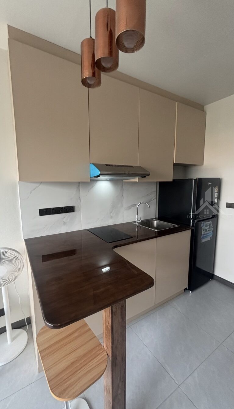 L-shaped dark wood bar counter with pendant lights and beige kitchen cabinets in a Treetops Pattaya condo